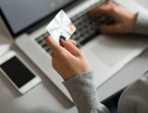 A close up of a woman's hand holding a credit card and using a laptop computer to apply for HomePro financing